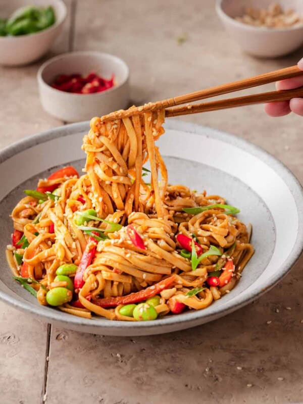 person using chopsticks to pick up sesame noodles from a bowl.