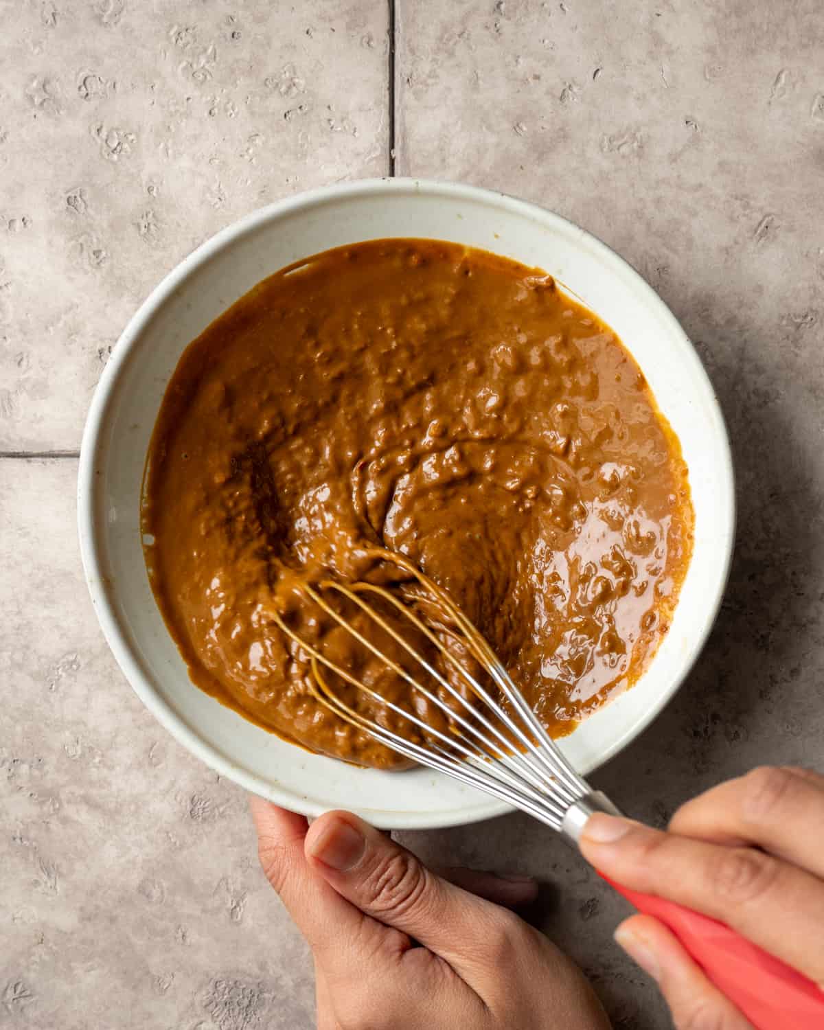 person whisking peanut sauce in a bowl.