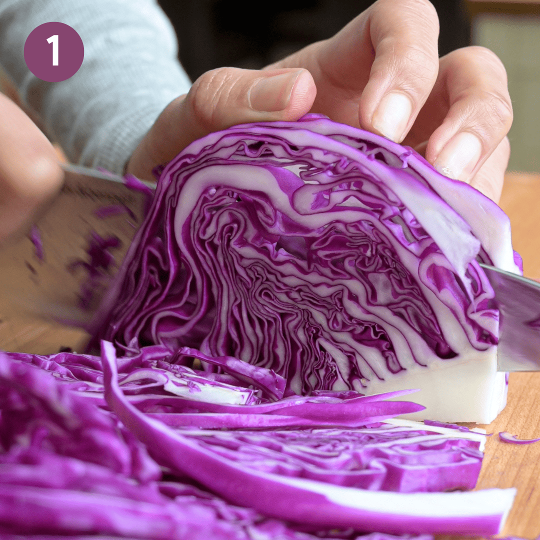 person thinly slicing red cabbage on a cutting board.
