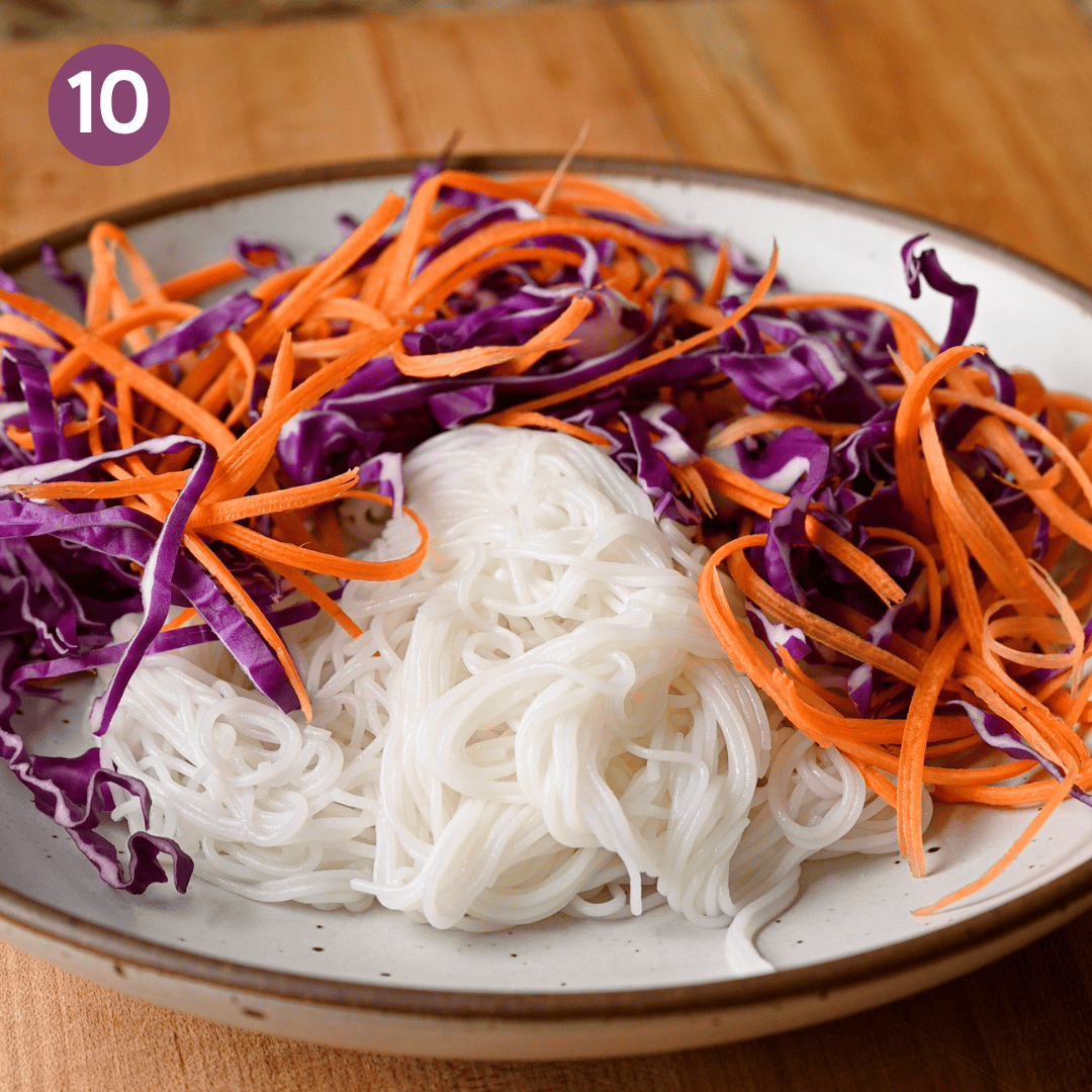 carrots and cabbage added to noodles in bowl.
