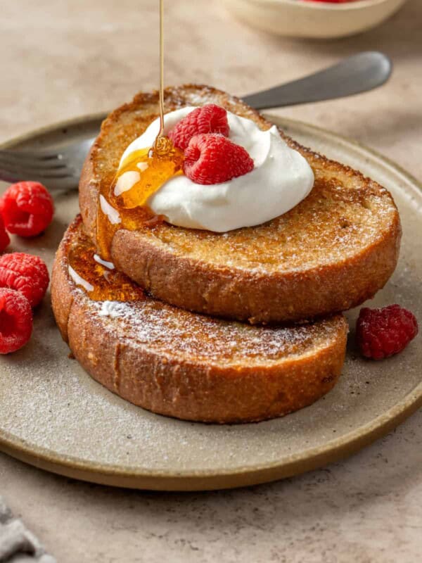 Side view of someone pouring maple syrup on two slices of vegan french toast.