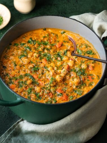 Chickpea soup with carrots and dill in a green Dutch oven with soup ladle in pot.