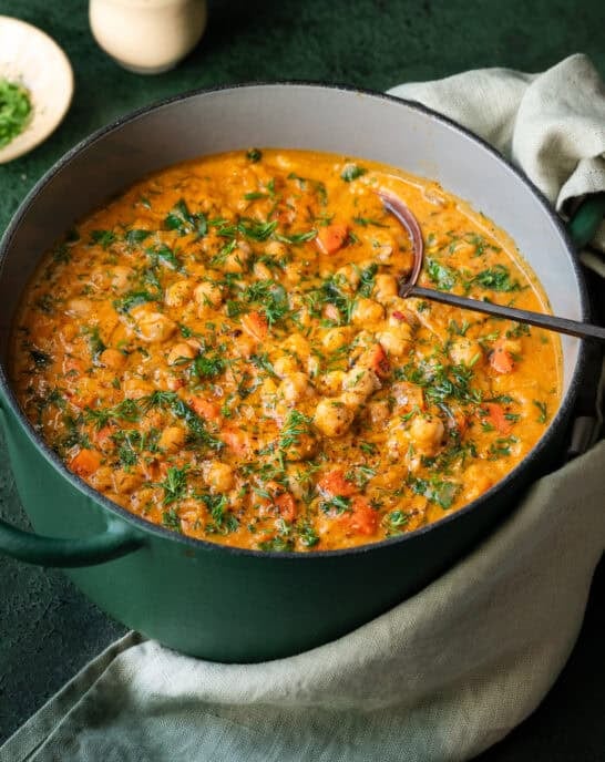 Chickpea soup with carrots and dill in a green Dutch oven with soup ladle in pot.