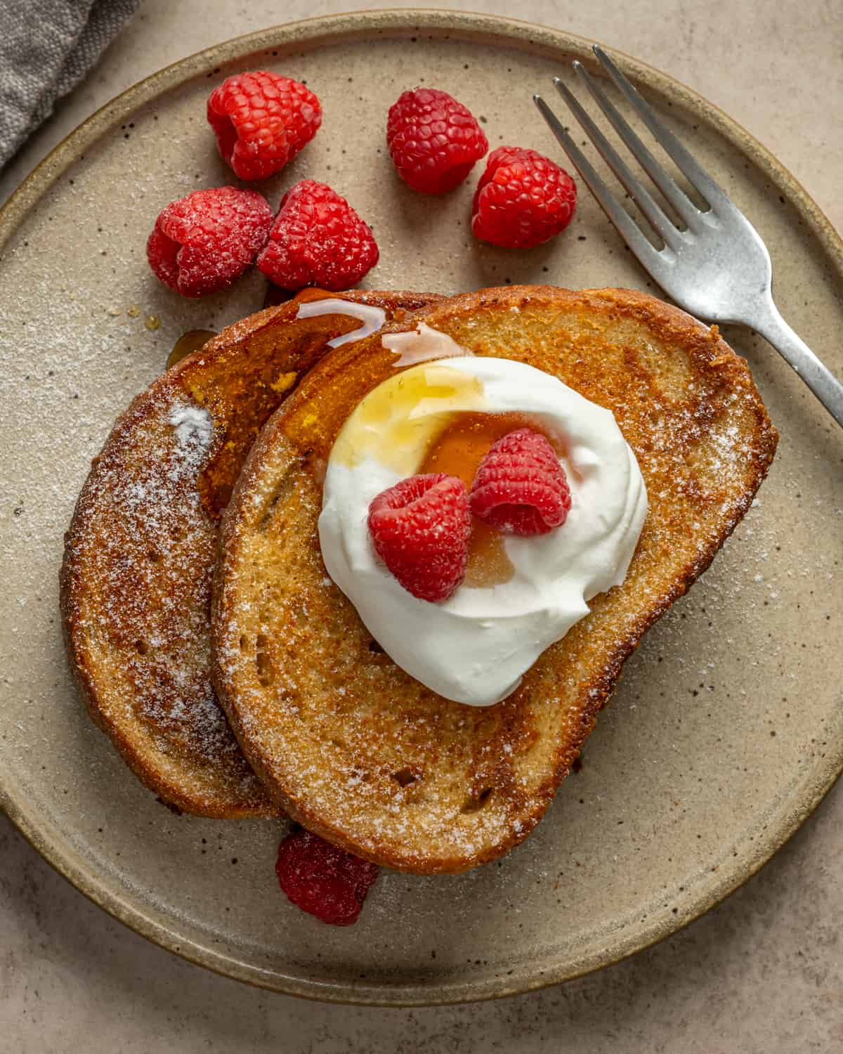 Overhead view of french toast with whipped topping, maple syrup and raspberries.