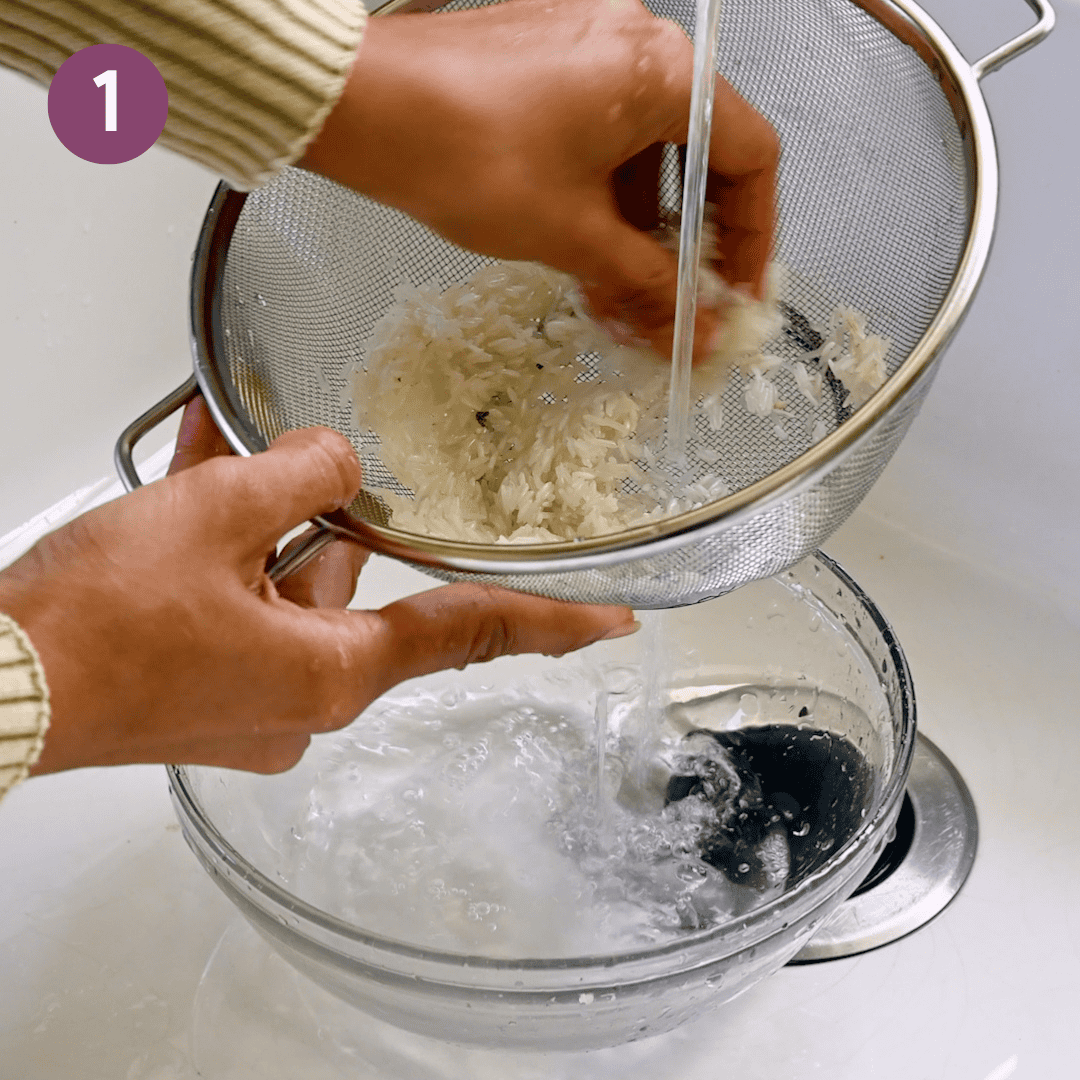 person rinsing rice in a colander in the sink.
