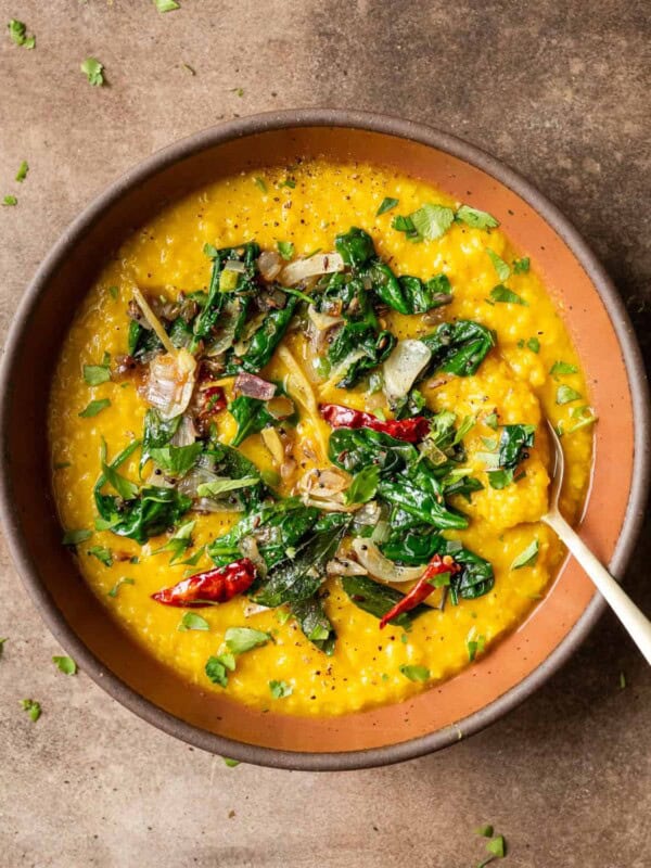 Dal palak in maroon bowl on a table.