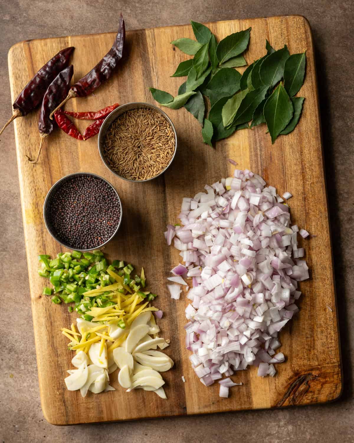 Tadka ingredients chopped and in small bowls on cutting board.