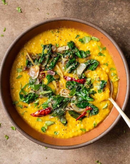 Dal palak in maroon bowl on a table.