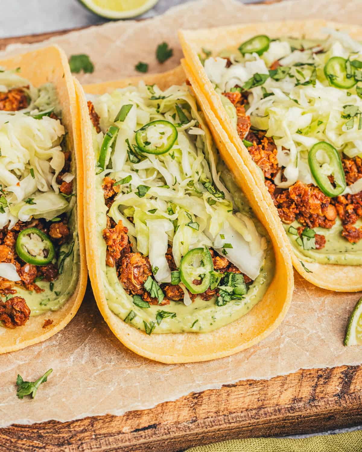 closeup on lentil tacos with avocado crema and cabbage slaw on a wooden cutting board. 