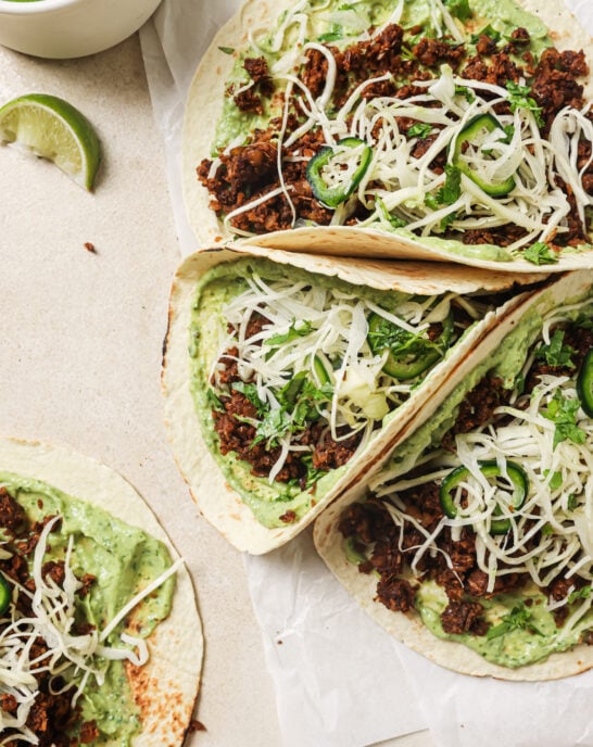 closeup of lentil tacos with avocado crema and slaw on parchment paper.