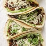 closeup of four lentil tacos with avocado crema and slaw on parchment paper.