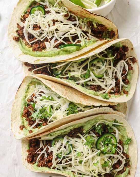 closeup of four lentil tacos with avocado crema and slaw on parchment paper.