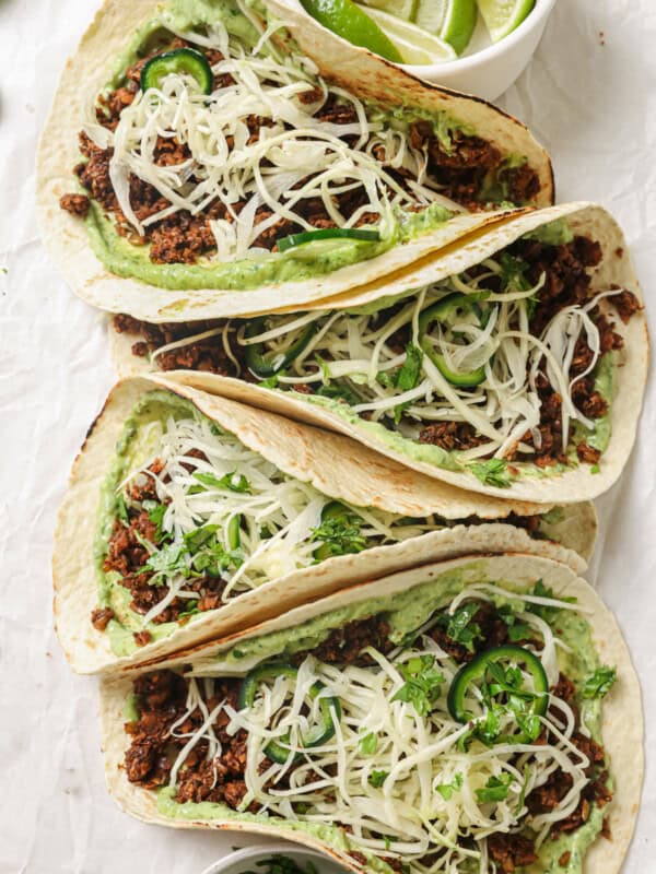 closeup of four lentil tacos with avocado crema and slaw on parchment paper.