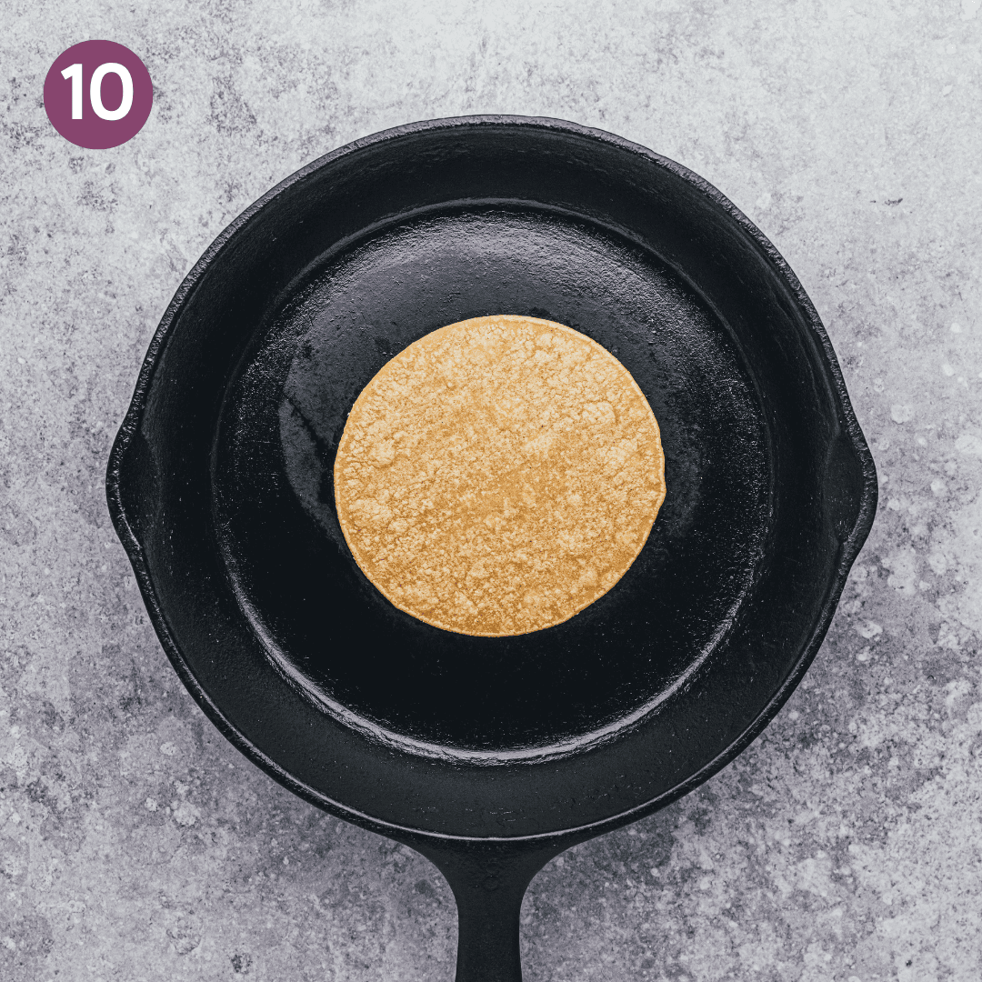 a corn tortilla being warmed up in a cast iron skillet.