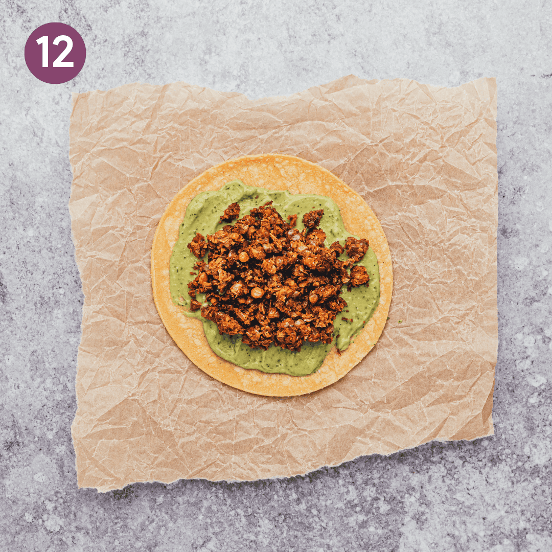 a corn tortilla topped with avocado crema and lentil taco meat on parchment paper.
