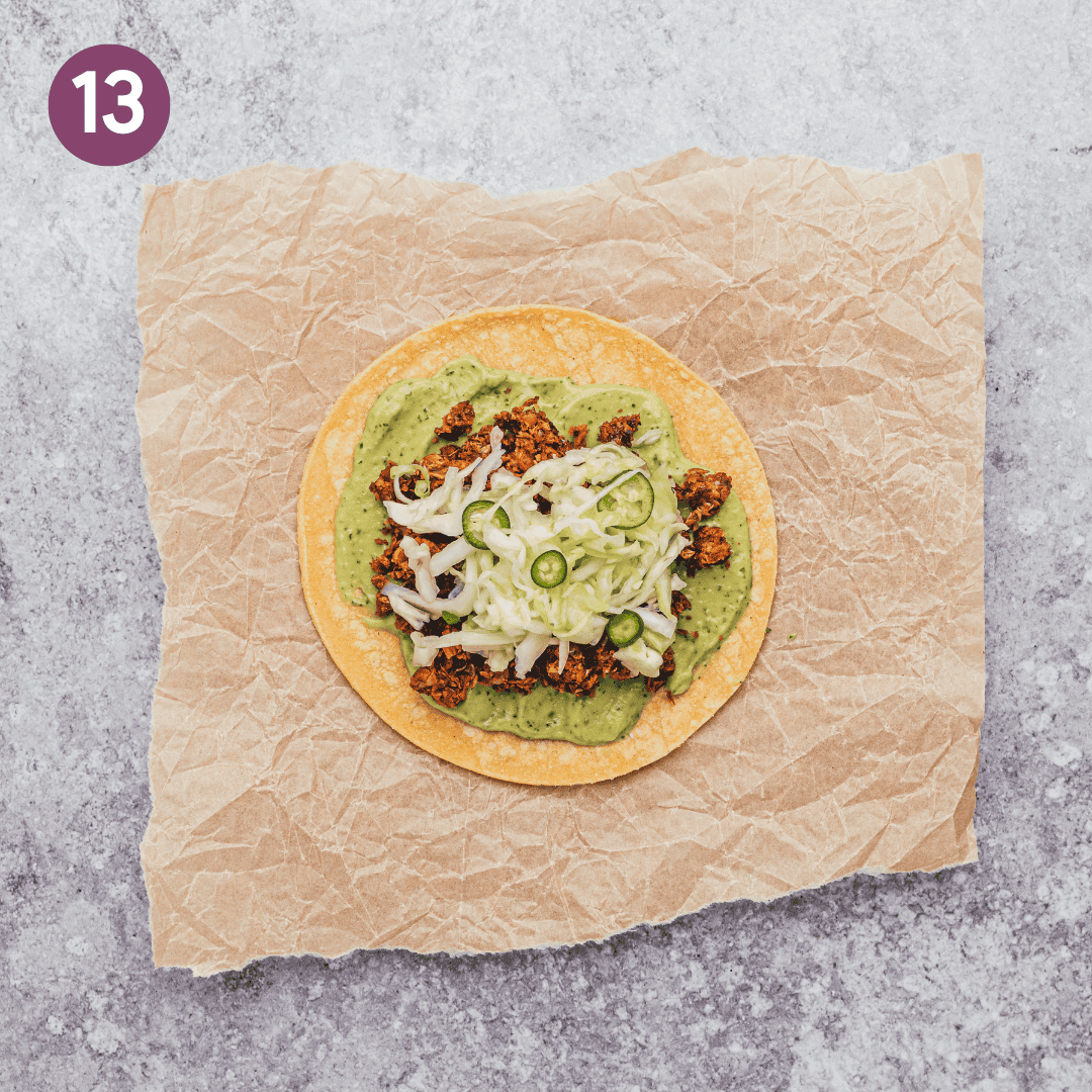 a corn tortilla topped with avocado crema, lentil taco meat, and slaw on parchment paper.