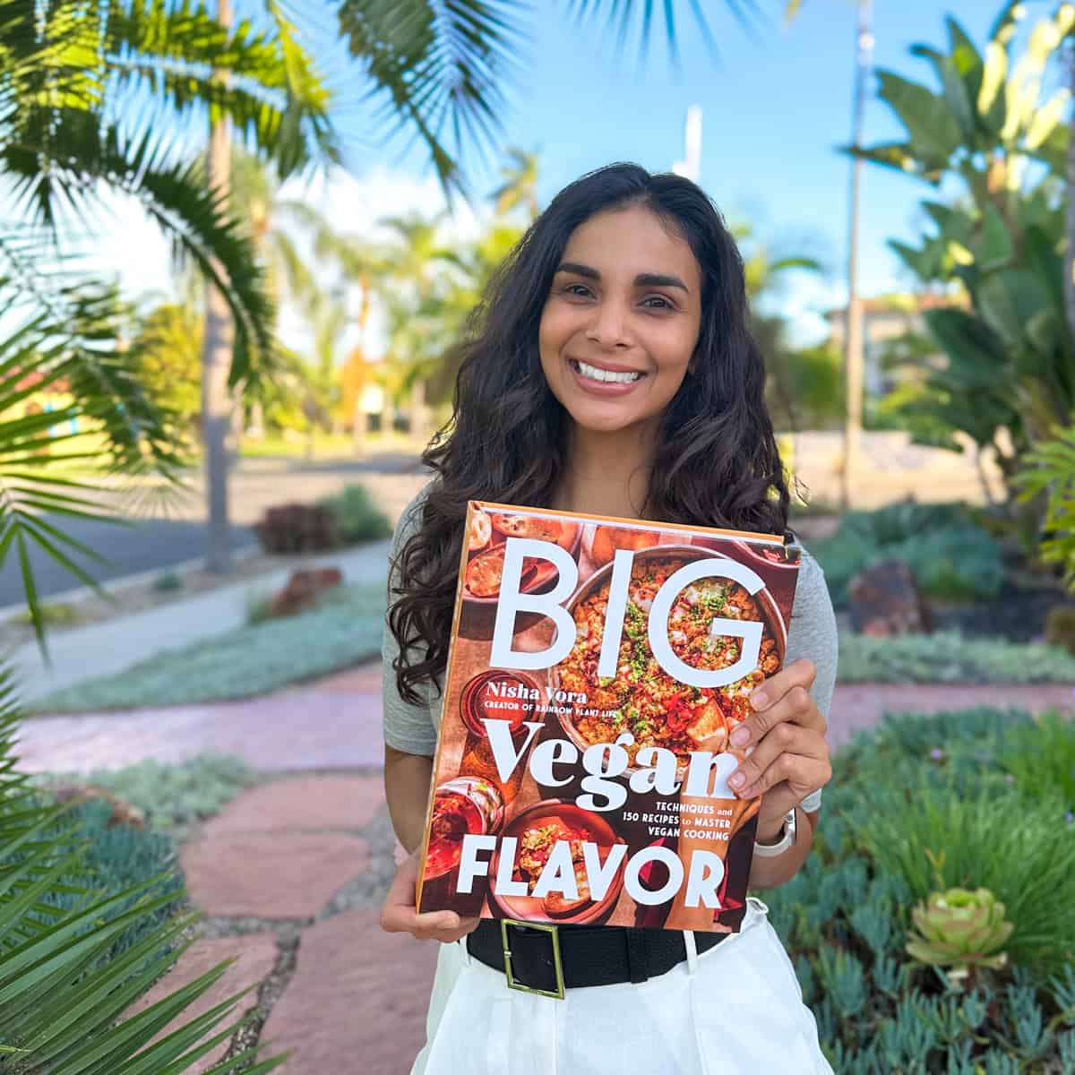 Nisha holding a copy of Big Vegan Flavor outside