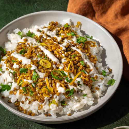 crispy Indian lentils on white rice with turmeric shallots in a shallow bowl on a green table.