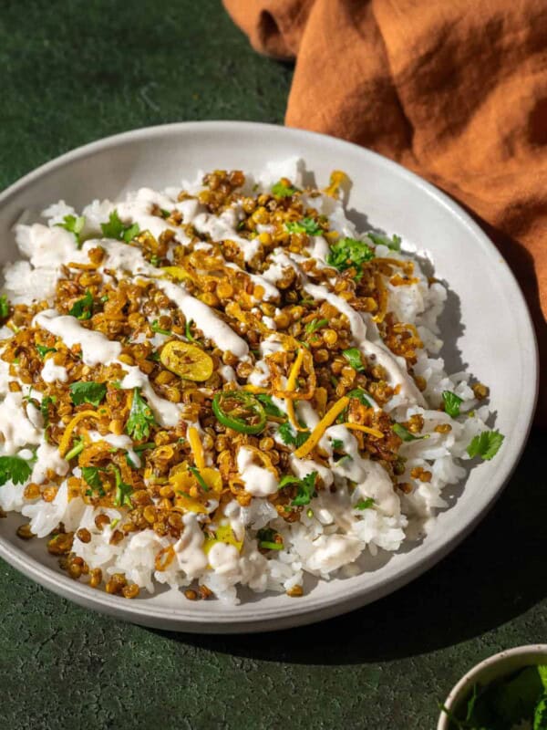 crispy Indian lentils on white rice with turmeric shallots in a shallow bowl on a green table.