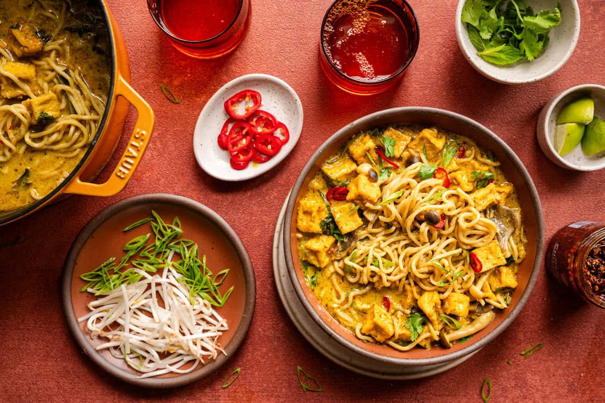 Malaysian curry noodle soup dinner scene on a red table.