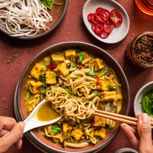 Malaysian curry soup with women's hands digging in with a spoon and chopsticks.