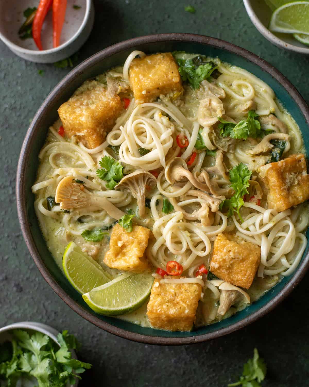 Malaysian curry noodle soup with fried tofu in a green bowl.