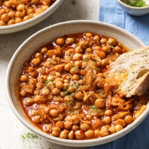 bowl of braised chickpeas with a chunk of crusty bread in it.