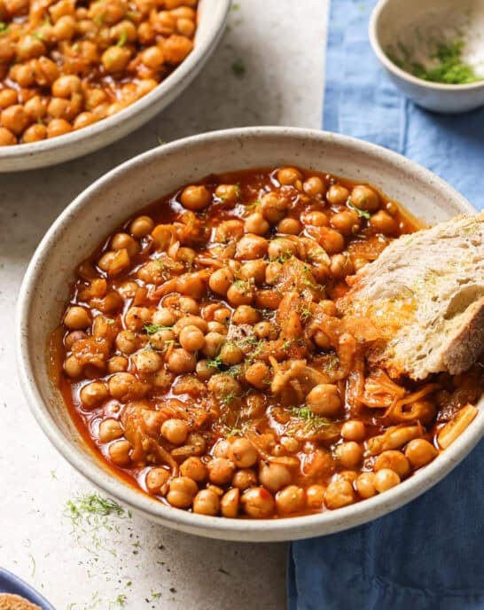 bowl of braised chickpeas with a chunk of crusty bread in it.