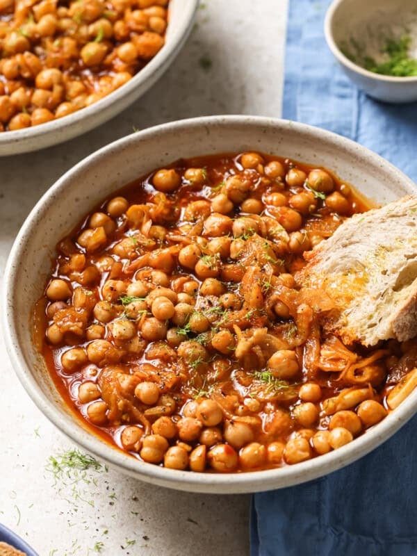 bowl of braised chickpeas with a chunk of crusty bread in it.