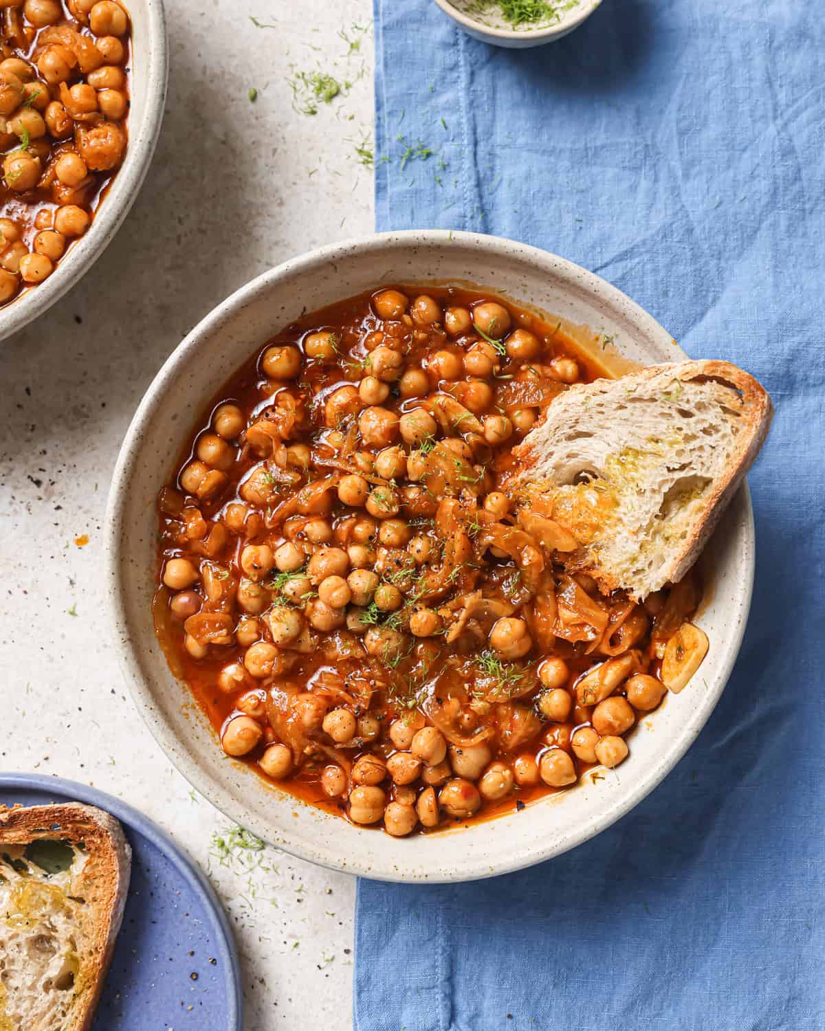 zoomed out overhead shot of braised chickpeas in a bowl with a chunk of crusty bread.