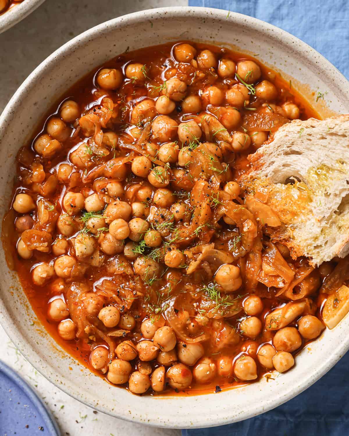 close up overhead shot of braised chickpeas in a bowl with a chunk of crusty bread.