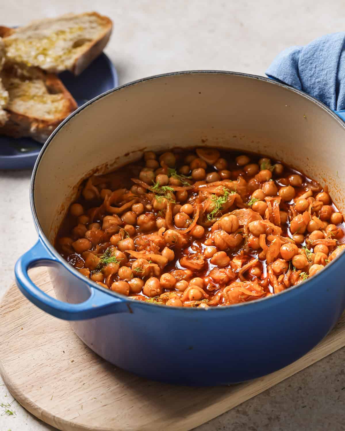 side view of a large pot of braised chickpeas next to a plate with crusty bread.