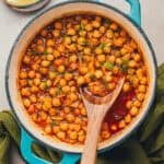 Wooden spoon in dutch oven filled with braised chickpeas.