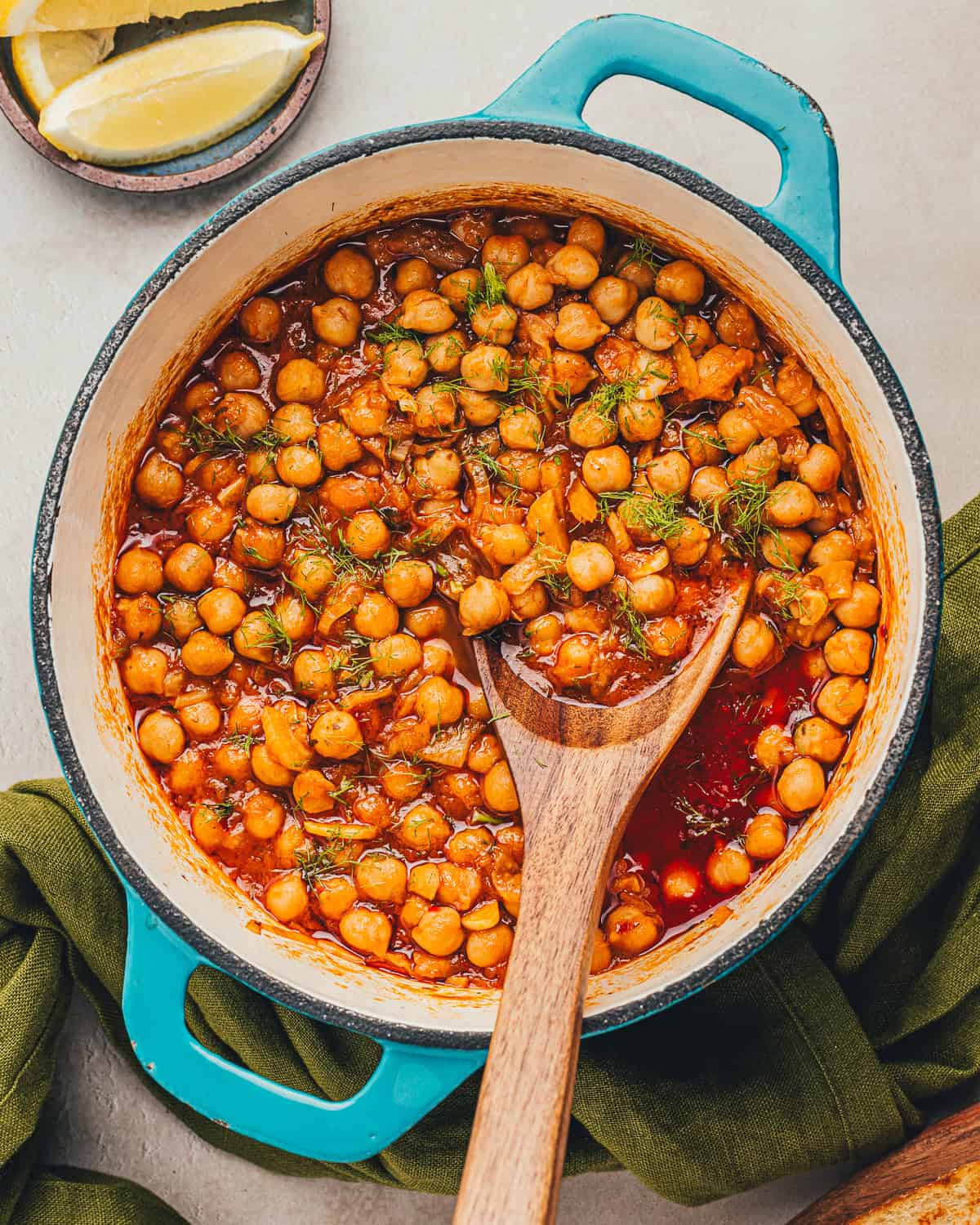 Wooden spoon in dutch oven filled with braised chickpeas.