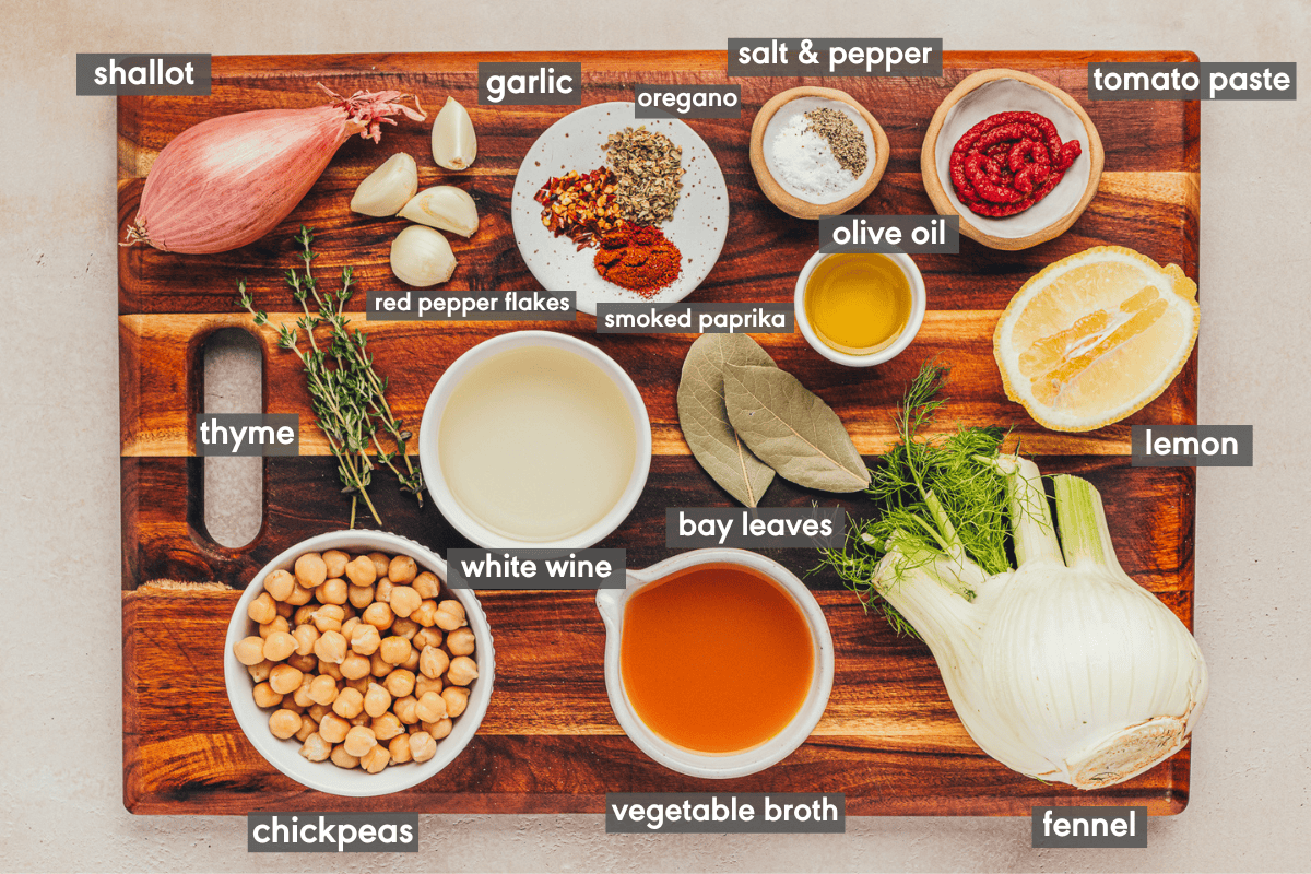 ingredients for braised chickpeas recipe on a wooden cutting board with ingredients labeled. 