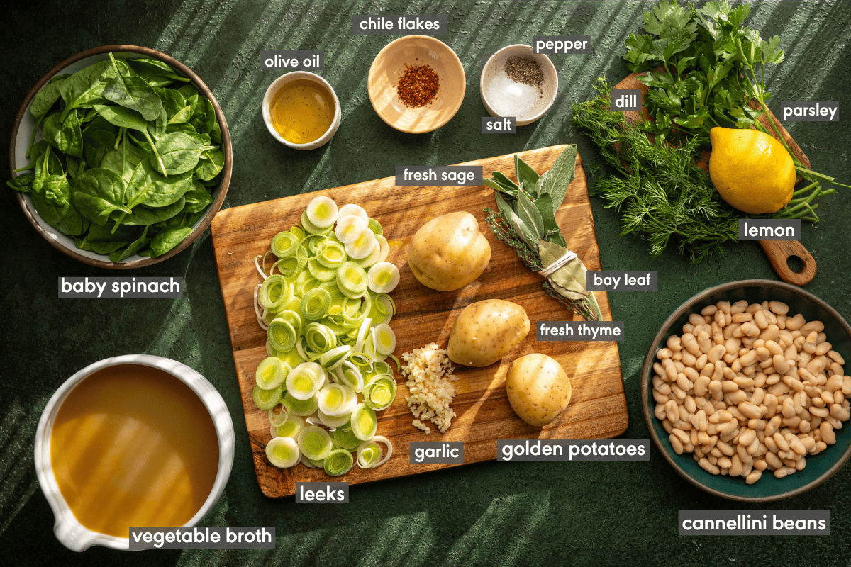 Vegan potato leek soup ingredients on a wooden cutting board and the green table it's on.