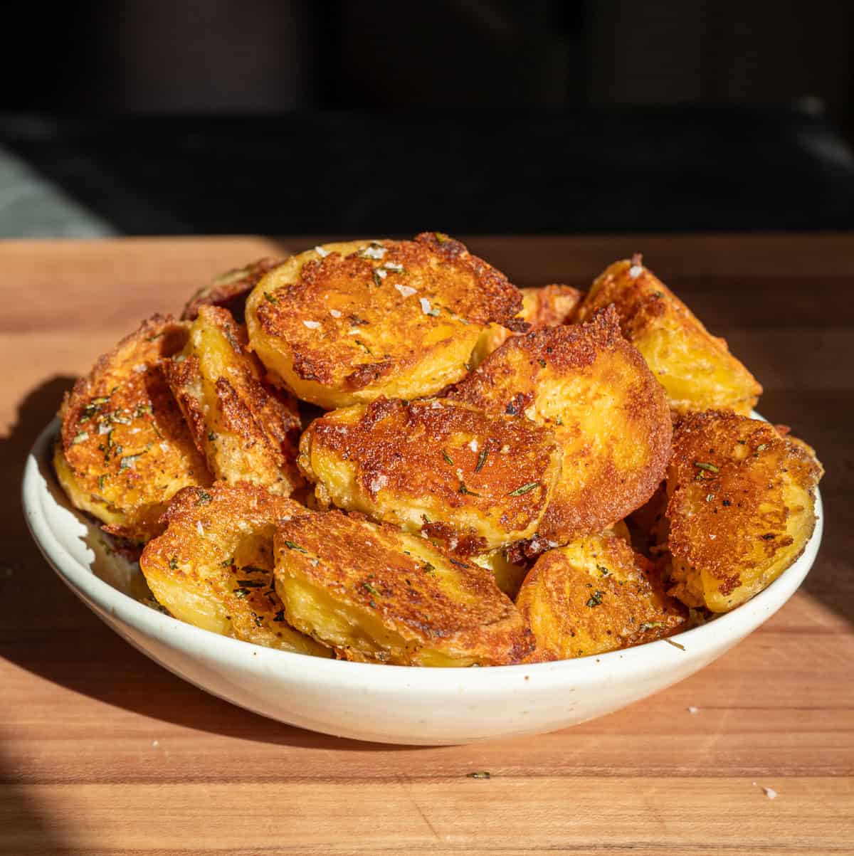 Crispy roasted potatoes in a large bowl on wood table.