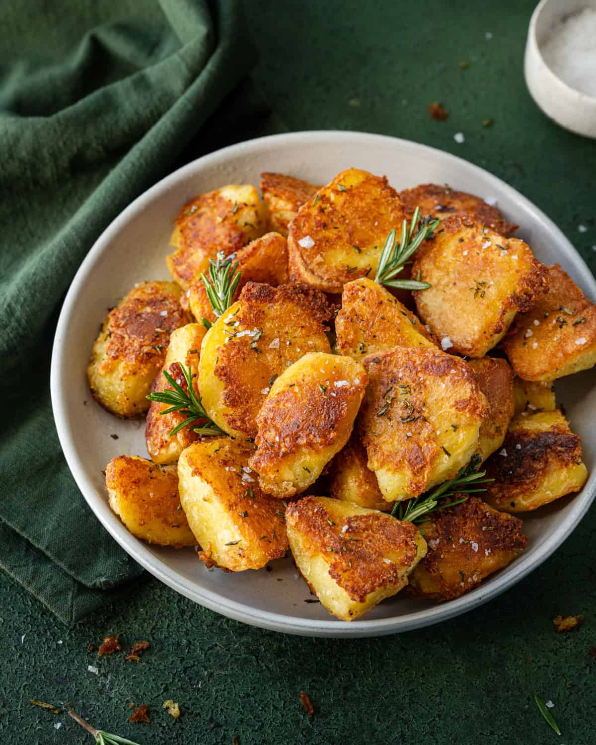 Crispy roasted potatoes with small rosemary sprigs on a tablecloth.