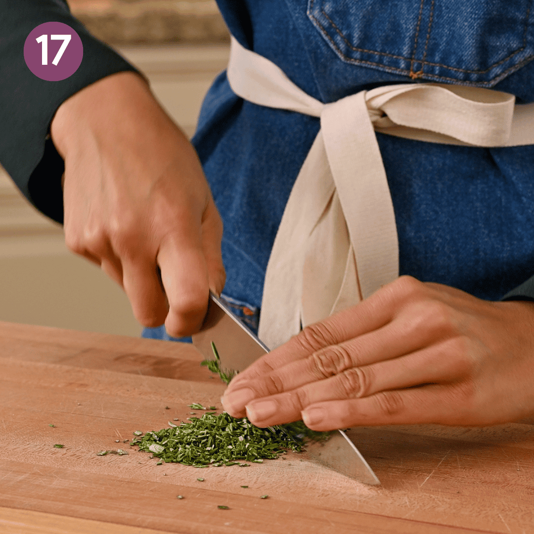 person chopping rosemary on a cutting board.