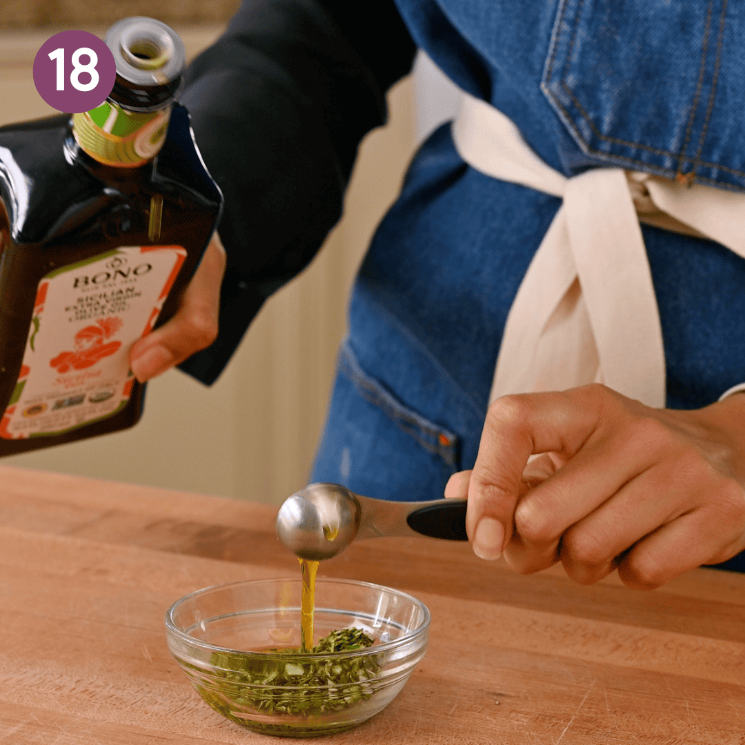 person pouring olive oil over rosemary in small bowl.