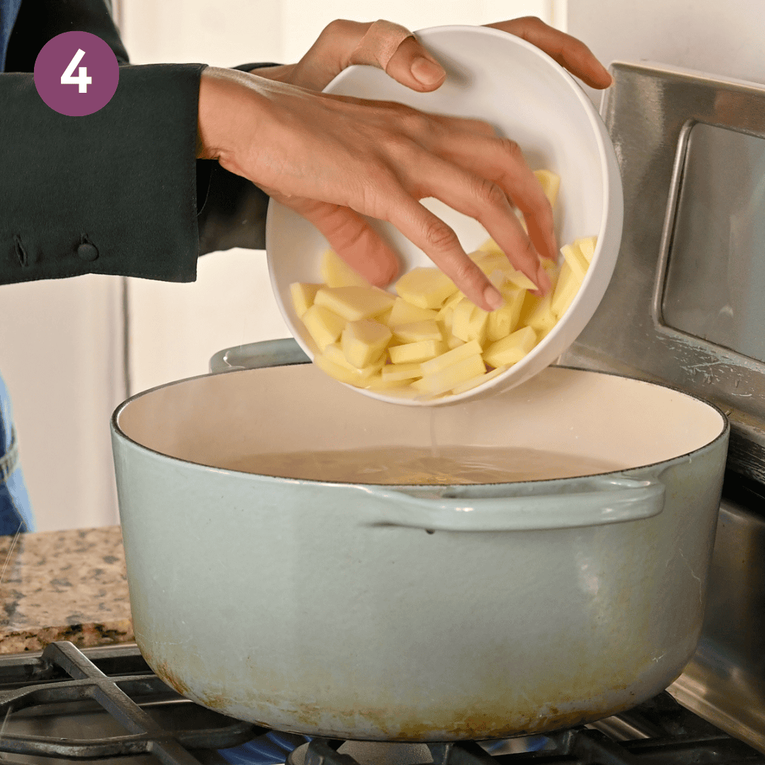 person adding russet potato into the pot with water and other potatoes.