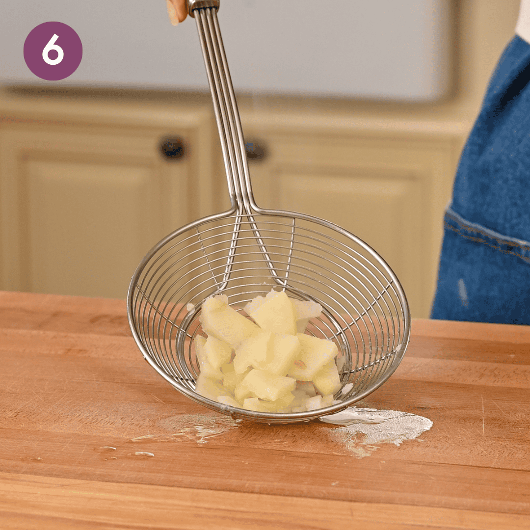 parboiled potatoes in a spider tool on a wooden cutting board.