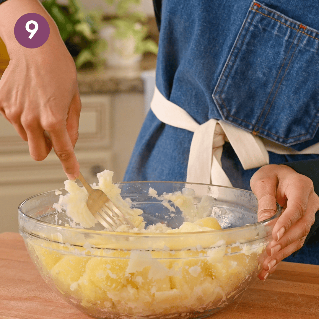 person masing the russet potato in the bowl.