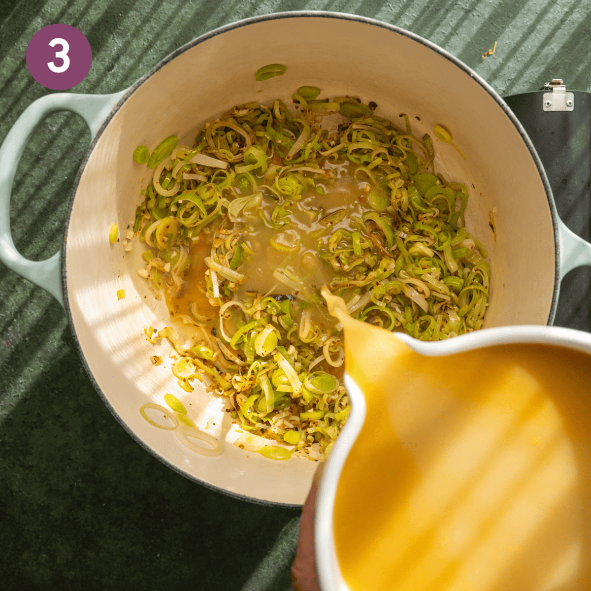 Person pouring in vegetable broth to leek mixture.