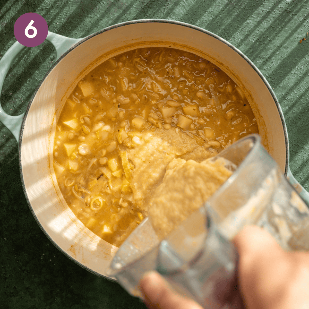 Person pouring the blended portion of the soup back into the pot.