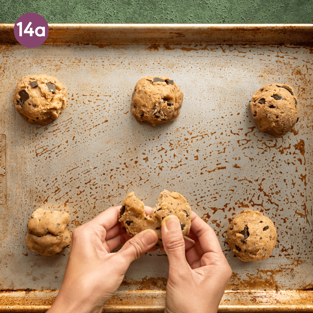 woman's hands tearing one cookie dough ball apart in half on a sheet pan.