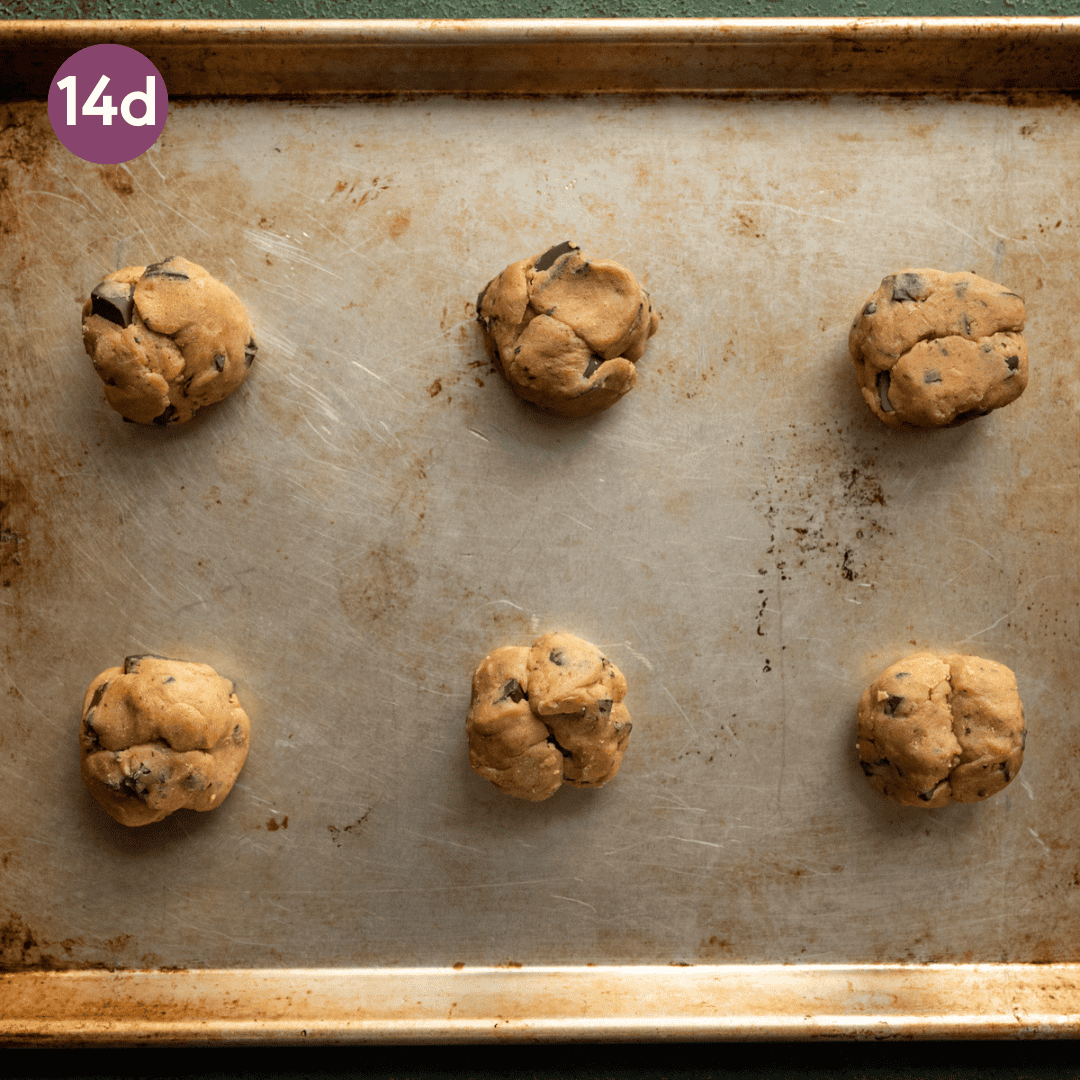 six chocolate chip cookie dough rounds on a sheet pan. 