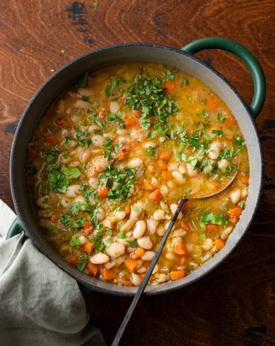 green dutch oven filled with white bean soup with carrots, ladle dug in.