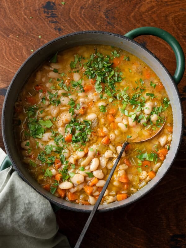 green dutch oven filled with white bean soup with carrots, ladle dug in.