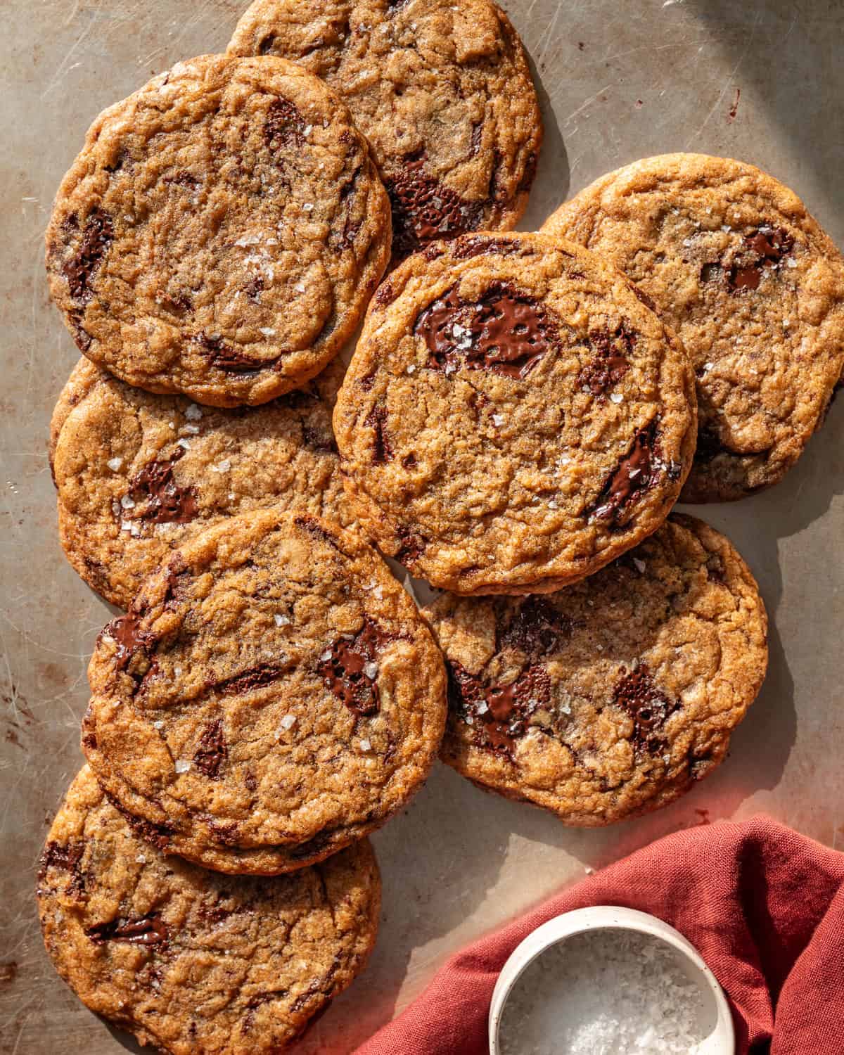 a pile of baked chocolate chip cookies on a baking sheet with a red towel.